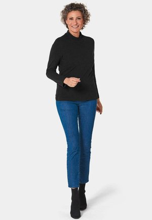 Schwarzes Langarm-Mockturtleneck-Oberteil, kombiniert mit blauen Slim-Fit-Jeans und schwarzen Ankle-Boots. Der Stoff wirkt glatt und leicht.