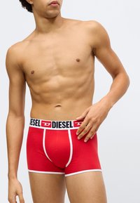 Sarkanas vīriešu bokserbikses ar baltām detaļām, elastīgu melnu jostu ar "DIESEL" logotipu un piegulošu fitu. Izgatavotas no mīksta, elastīga materiāla.