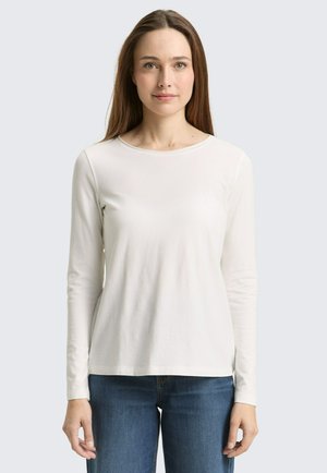 Wit shirt met lange mouwen en ronde hals, gemaakt van zachte stof, met een ontspannen pasvorm en geribbelde textuur, gecombineerd met een blauwe spijkerbroek.