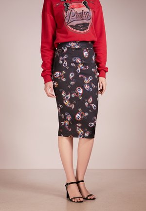 Vrouw draagt een zwarte rok tot kniehoogte met kleurrijke paisley-patronen, een rood sweatshirt met letters en zwarte enkellaarsjes met riempjes.