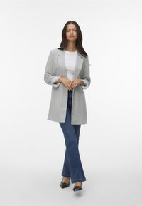 Jasnoszary żakiet z podwiniętymi rękawami, wyraźnie zaznaczonymi klapami, kieszeniami naszytymi, zestawiony z rozszerzającymi się ciemnymi dżinsami i błyszczącymi czarnymi balerinami.
