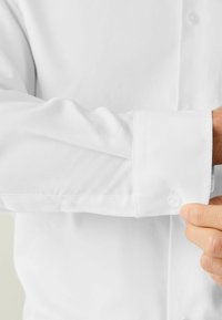 Biela košeľa s dlhými rukávmi, ktorá má hladkú textúru, rozopínateľné manžety na gombíky a priliehavý strih, prezentujúca čistý a klasický vzhľad.