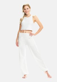 Top corto bianco e pantaloni a gamba larga, entrambi in tessuto morbido. I pantaloni presentano un'alta vita elastica e tasche laterali.