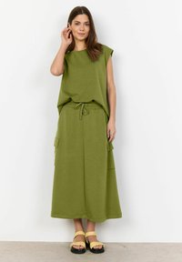 Green, relaxed-fit top with short sleeves paired with a matching long skirt featuring cargo pockets and an elastic waistband. Strappy yellow sandals.