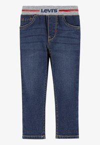 Jean en denim bleu foncé avec une ceinture élastique grise présentant un motif rayé rouge et bleu. Cinq poches et détails de couture jaune.