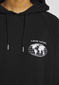 Black hooded sweatshirt made of textured fabric. Features a white globe graphic and "LOVE NATION" text on the chest. Silver aglets on drawstrings.