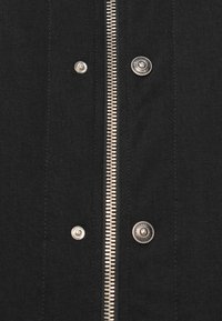 Chaqueta de denim negra con cremallera plateada, botones a presión y costuras visibles. La textura es resistente con un diseño clásico.