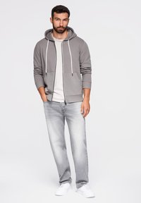 Szara bluza z zamkiem i sznurkiem na kapturze, noszona na jasnej koszulce. Połączona z jasnoszarymi dżinsami i białymi trampkami. Prosty design i luźny krój.