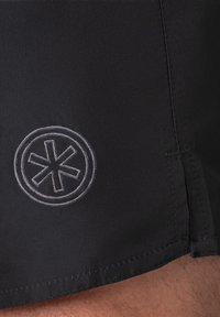 Black swim shorts made of smooth fabric featuring a circular logo with a star pattern in light gray embroidery. Side seam finish is neat.