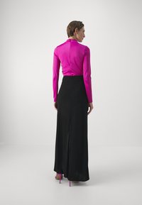 Lunga gonna nera con uno spacco alto abbinata a una maglietta attillata rosa a maniche lunghe, caratterizzata da una texture liscia e un design elegante. Scarpe con tacco rosa.