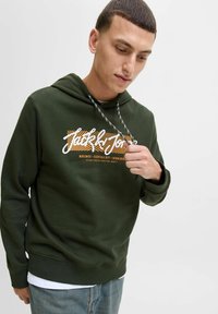 Grøn sweatshirt med hætte, der har et hvidt og orange grafisk logo. Inkluderer snore med sort og hvidt mønster.