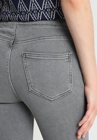 Jeans de mezclilla gris con un único bolsillo trasero en forma de diamante, costuras sutiles y una textura suave.