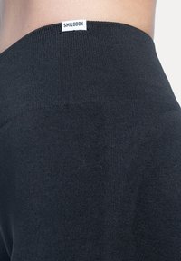 Zwarte legging met een geribbelde tailleband, voorzien van een gladde textuur en een klein merkembleem aan de voorkant van de tailleband.