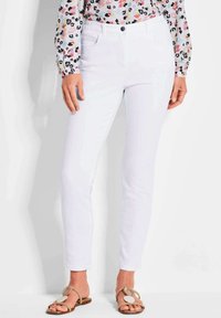 Witte skinny jeans van katoen, met een knoopsluiting aan de voorkant en zakken. Gemaakt in combinatie met een langmouwen bloempatronen top en sandalen.