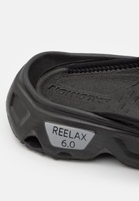 Črne zmysline sandale z teksturiranim podplatom, oblazinjenim stopalom in kovinsko oznako "REELAX 6.0." Gladko notranje dno.