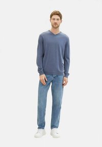 Pulover tricotat albastru cu decolteu în V, asortat cu blugi albastru deschis și adidași albi. Ținuta are croială lejeră și textură fină.