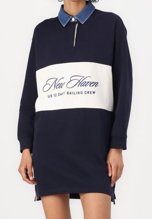 Robe bleu marine à manches longues avec panneau blanc et texte "New Haven US 12 Gant Sailing Crew", avec col en denim bleu et bouton.