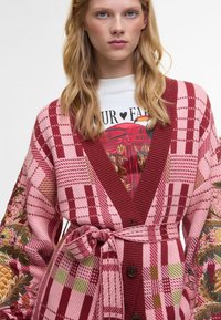 Πλεκτό μπουφάν με καρό μοτίβο σε αποχρώσεις ροζ και κόκκινου, με λουλουδάτη κεντημένη διακόσμηση στα μανίκια και ταιριαστό ζωνάκι.