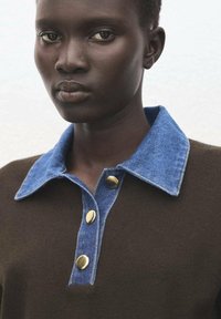 Suéter marrón con cuello de mezclilla y grandes botones dorados. Primer plano que muestra la textura y los detalles de la artesanía de la prenda.