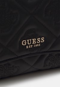 Sac en cuir noir matelassé avec des motifs embossés et le logo métallique doré "GUESS EST 1981".