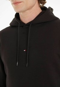 Felpa nera in cotone. Presenta un cappuccio con cordino, ricamo del logo sulla parte anteriore e un piccolo emblema tricolore sul petto.