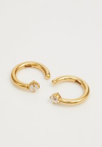 Boucles d'oreilles en or en forme de créole avec une finition lisse et polie, ornées d'un petit cristal rond sur un côté. Conçues avec une forme ouverte.