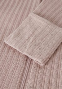 Tissu tricoté rose clair avec une texture côtelée et de petits motifs répétitifs. Comprend une fermeture éclair et un détail de poignet replié.
