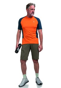 Oranžové a námořnické sportovní tričko s krátkým rukávem, spárované s olivově zelenými šortkami. Krátké ponožky a šedé sportovní boty, držící černou láhev na vodu.