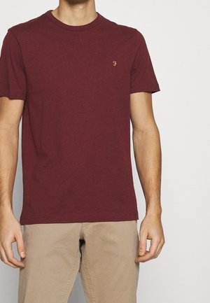 T-shirt corto bordeaux in cotone, con colletto rotondo e un piccolo logo giallo sul lato sinistro del petto. Morbido, con una texture liscia.