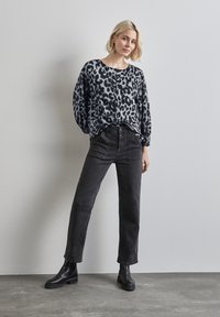 Chemisier à boutons avec imprimé léopard noir et gris, associé à un jean taille haute noir et des bottines, sur fond uni.