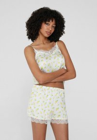 Witte satijnen pyjama set met gele citroenprint. Het tanktop heeft kantafwerking, terwijl de shorts een elastische tailleband en een kanten zoom hebben.