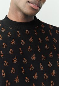 Maglione nero con collo a coste, caratterizzato da un motivo completo di decorazioni natalizie arancioni e fiocchi di neve, dalla texture liscia.