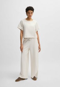 Light beige crop top with short sleeves, paired with wide-leg pants in matching color, featuring drawstring waist and smooth fabric texture.