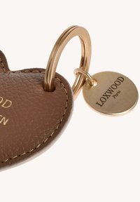 Porte-clé en cuir marron en forme de cœur, fixé à des anneaux en or avec une étiquette ronde en or gravée "Loxwood Paris".