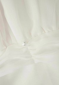 Biała tkanina z szyfonu o delikatnym układaniu, z perłowym akcentem przy zgromadzonej szwie w talii, eksponująca lekką i zwiewną teksturę.