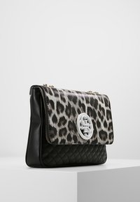 Černá kožená kabelka s klopou se vzorem leopardí kůže. Má prošívanou texturu a kulatý bílý logotyp na přední straně.