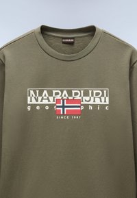 Oliven grøn langærmet T-shirt med rund hals, der har et hvidt logo og et lille norsk flag mærke, lavet af struktureret bomuldsmateriale.