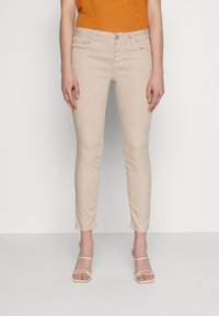 Jean skinny beige en mélange de coton, avec fermeture éclair, poches avant et texture lisse. Fini avec des détails de couture subtils.