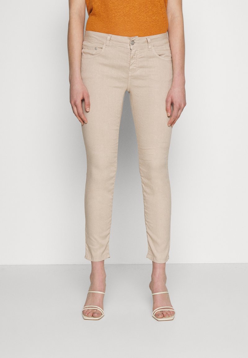 Jean skinny beige en mélange de coton, avec fermeture éclair, poches avant et texture lisse. Fini avec des détails de couture subtils.