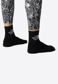 Sorte crew sokker med ribbet tekstur som har hvit "The North Face"-logo. Grå, camo-mønstrede leggings synlige over.