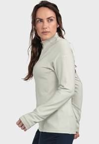 Hellgrünes Langarm-T-Shirt mit hohem Kragen und halbem Reißverschluss, das über eine gerippte Textur und ein kleines Logo auf der Schulter verfügt.