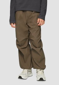 Bruine elastische taillebroek met een losse pasvorm, gemaakt van zachte stof. Gepaard met wit en grijs sneakers, met gestructureerde paneeldetails.