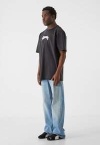 Sort oversized T-shirt med hvid grafik, parret med lyseblå vide bukser og sorte sportsko. Glat stof, afslappet pasform.