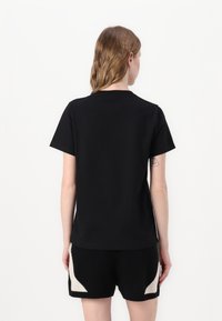 T-shirt noir à manches courtes avec un col rond et en tissu doux, porté avec un short noir avec un motif géométrique crème.