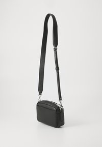 Black textured leather crossbody bag with a rectangular shape, silver zippers, and an adjustable strap. Minimalist design with no visible patterns.