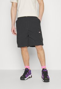 Black cargo shorts with multiple pockets, adjustable waistband, and contrasting stitching. Paired with black and purple athletic shoes, neon pink socks.