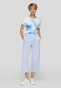 Weißes T-Shirt mit blauem floralen Grafikdesign, kombiniert mit weit geschnittenen Hosen in Blau und Weiß mit vertikalen Streifen und weißen Sneakers.
