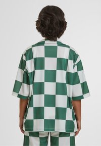 Camicia a maniche corte a scacchi verde e bianco, realizzata in un tessuto liscio, con colletto classico e vestibilità rilassata.