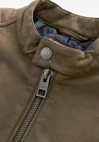 Primer plano de una chaqueta de cuero marrón con un alto cuello, herrajes de plata y una superficie texturizada. Incluye un zipper visible y un detalle de botón a presión.