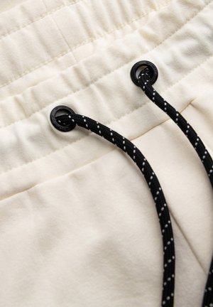 Tela color crema con una textura suave, que presenta una cintura fruncida y un cordón negro con puntos blancos.